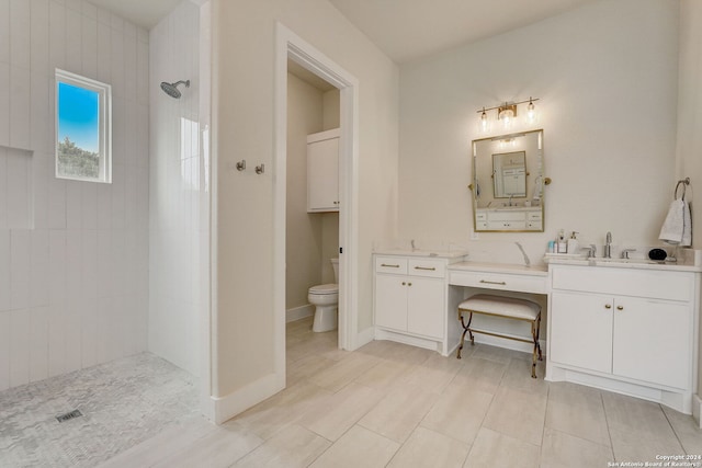 bathroom with dual bowl vanity, tile flooring, tiled shower, and toilet