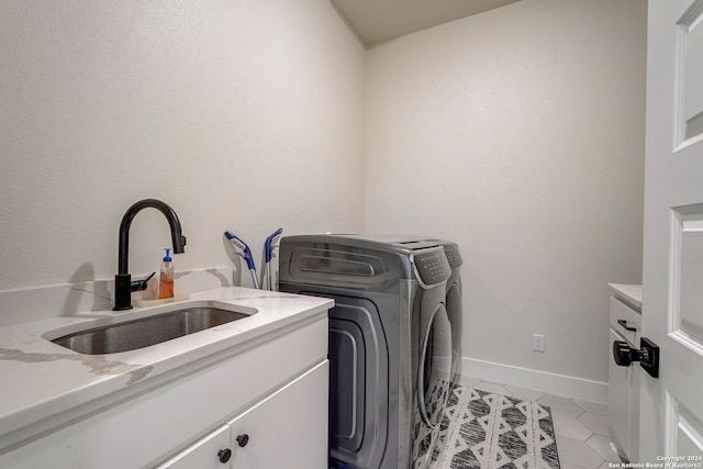 clothes washing area with sink, washing machine and clothes dryer, light tile flooring, and cabinets