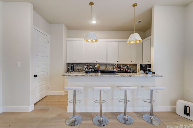 kitchen with white cabinetry, hanging light fixtures, light wood-type flooring, light stone counters, and backsplash