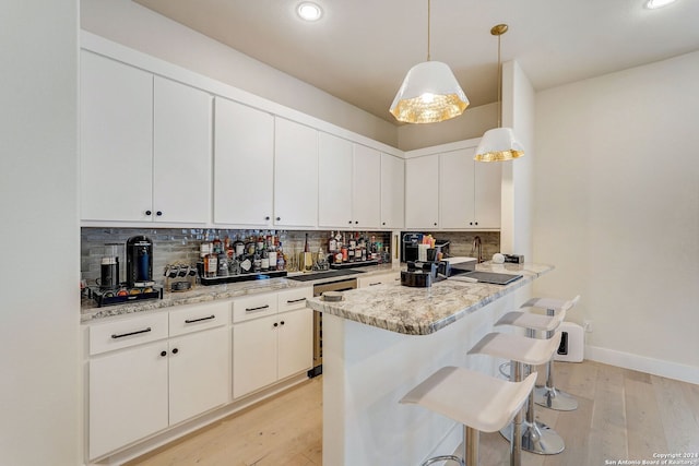 kitchen with decorative light fixtures, a kitchen breakfast bar, light hardwood / wood-style floors, and backsplash