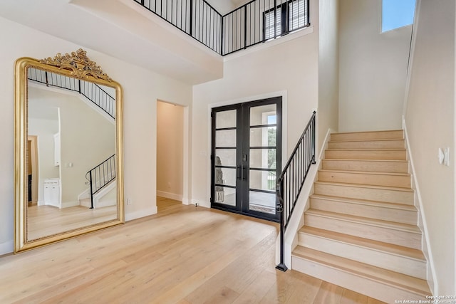 entrance foyer with a towering ceiling, light hardwood / wood-style floors, and french doors