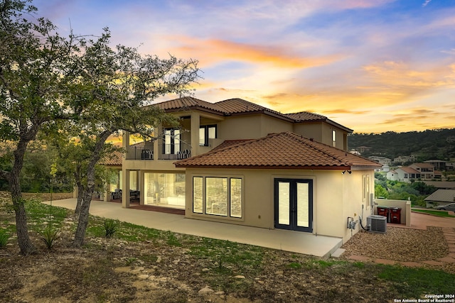 back house at dusk featuring central AC, a balcony, and a patio