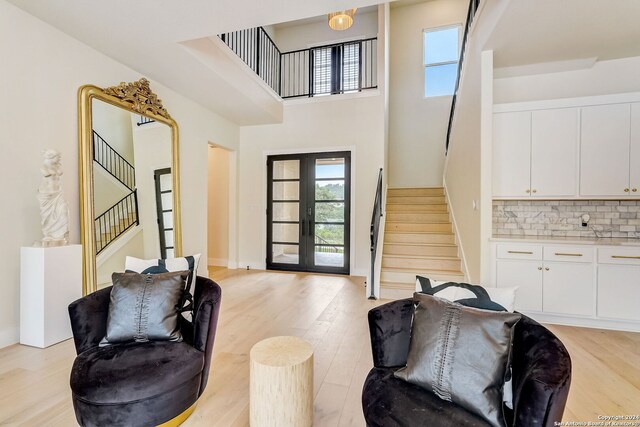 living room featuring a high ceiling, light hardwood / wood-style floors, and french doors