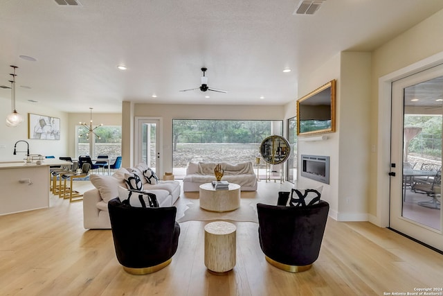 living room featuring sink, light wood-type flooring, and ceiling fan with notable chandelier