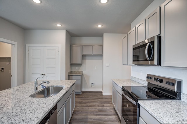 kitchen featuring appliances with stainless steel finishes, gray cabinetry, dark wood-type flooring, light stone counters, and sink