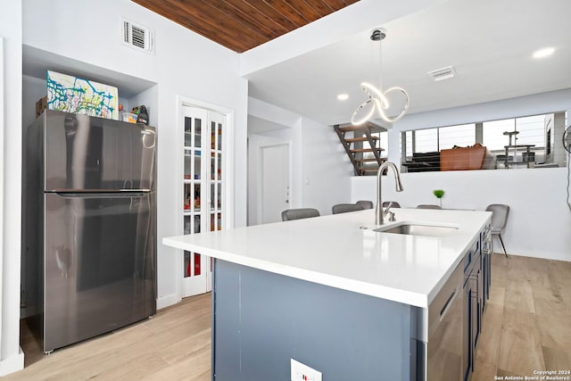 kitchen featuring an island with sink, hanging light fixtures, stainless steel fridge, and light hardwood / wood-style flooring