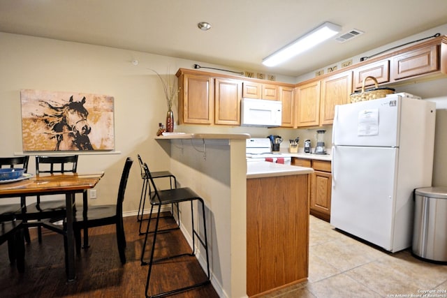 kitchen with light tile flooring, kitchen peninsula, and white appliances