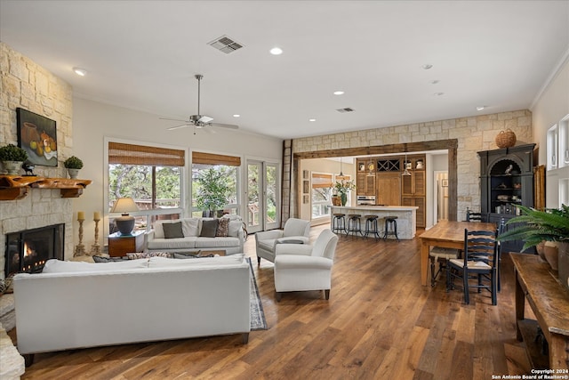 living room with ceiling fan, a stone fireplace, hardwood / wood-style flooring, and crown molding