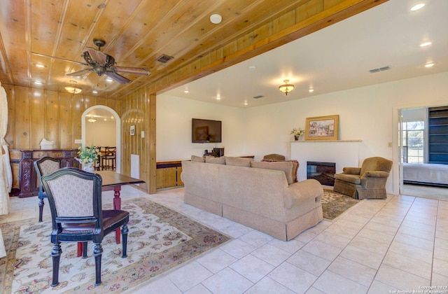 living room with wooden ceiling, wooden walls, light tile flooring, and ceiling fan