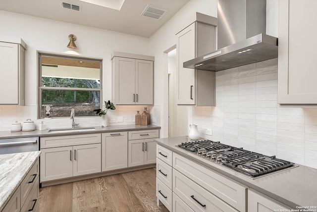 kitchen featuring backsplash, sink, wall chimney exhaust hood, light wood-type flooring, and stainless steel appliances