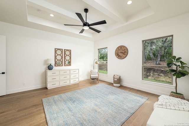 living area featuring beam ceiling, a tray ceiling, ceiling fan, and wood-type flooring