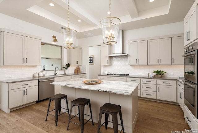 kitchen featuring sink, a center island, wall chimney exhaust hood, a chandelier, and appliances with stainless steel finishes