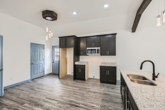 kitchen featuring decorative light fixtures, wood-type flooring, light stone countertops, beamed ceiling, and sink