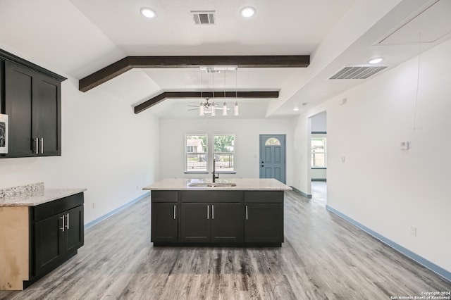 kitchen featuring ceiling fan, vaulted ceiling with beams, light wood-type flooring, sink, and a kitchen island with sink