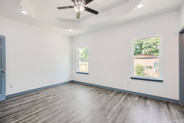 spare room with ceiling fan, a raised ceiling, a healthy amount of sunlight, and hardwood / wood-style floors