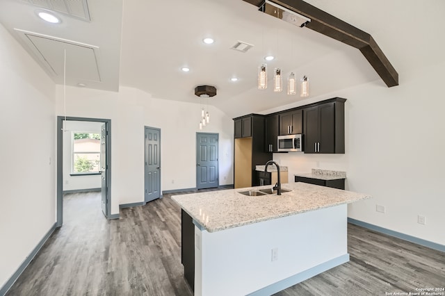 kitchen featuring light stone counters, light hardwood / wood-style flooring, a kitchen island with sink, vaulted ceiling with beams, and sink