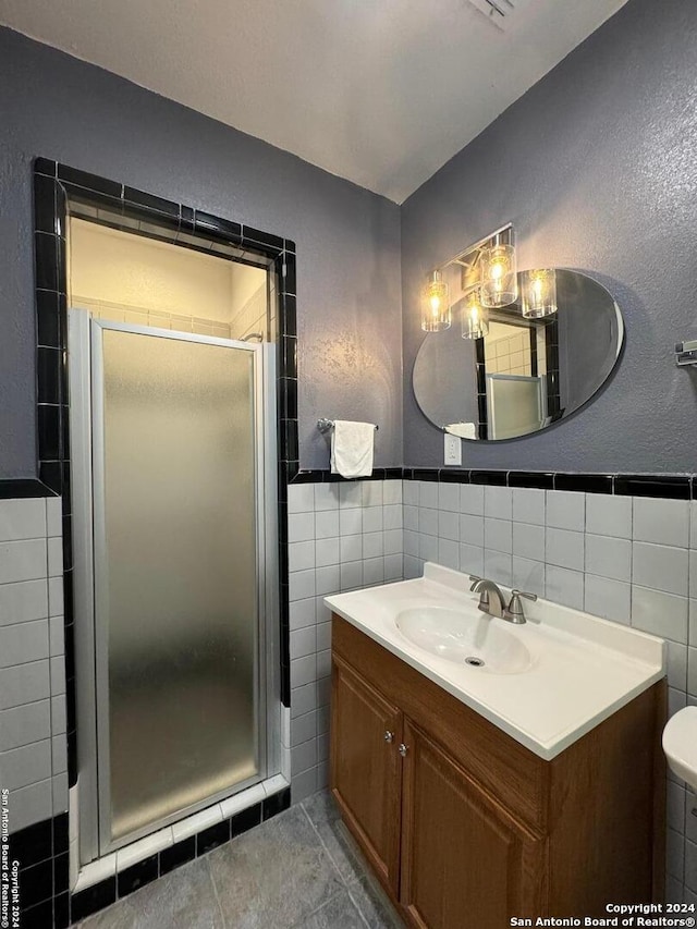 bathroom featuring tile flooring, a shower with shower door, oversized vanity, and tile walls