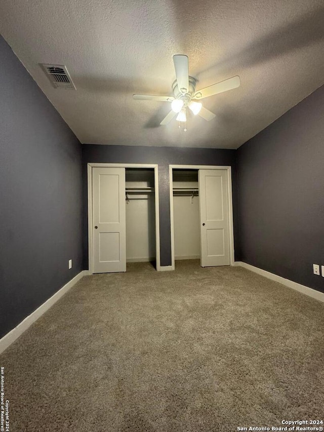 unfurnished bedroom with two closets, ceiling fan, carpet floors, and a textured ceiling