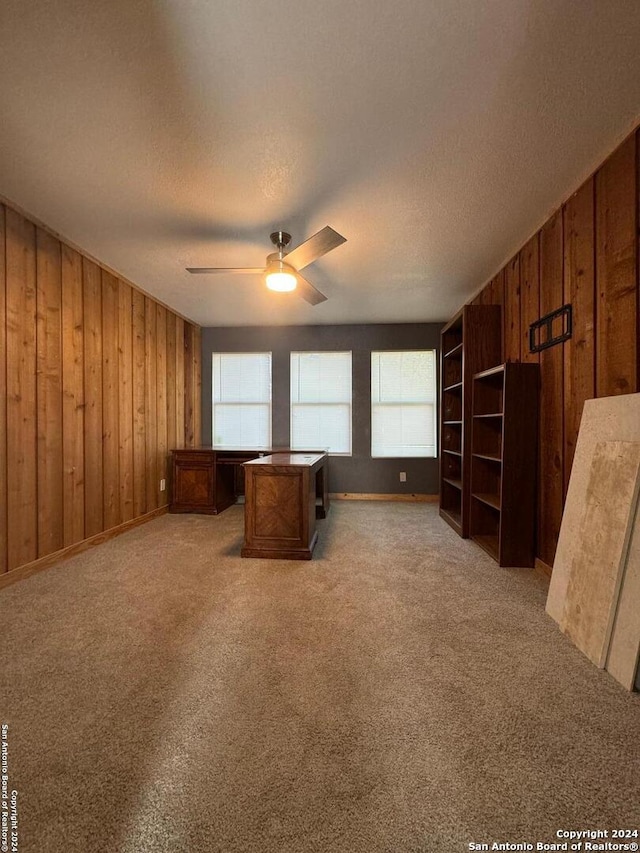 unfurnished living room with a textured ceiling, carpet flooring, wooden walls, and ceiling fan