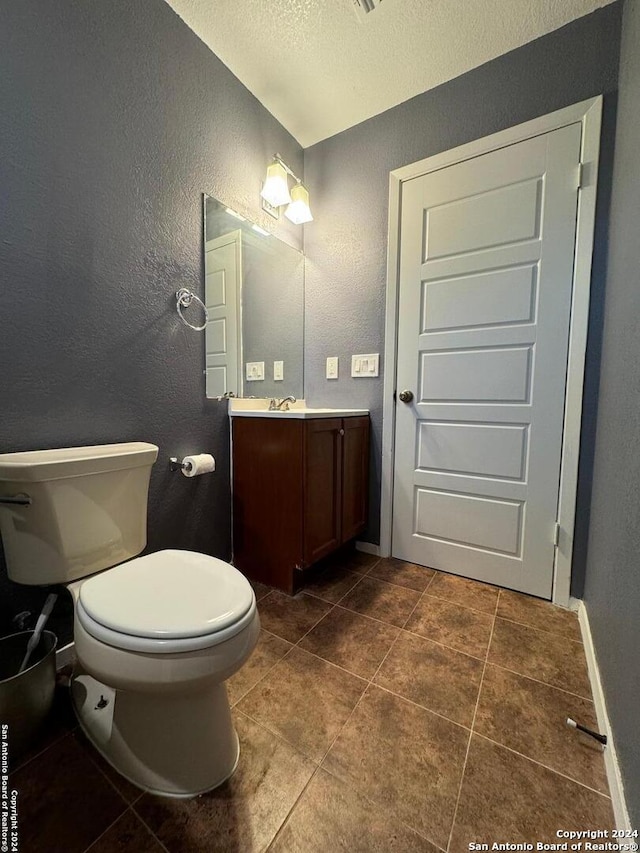 bathroom with tile flooring, a textured ceiling, toilet, and vanity