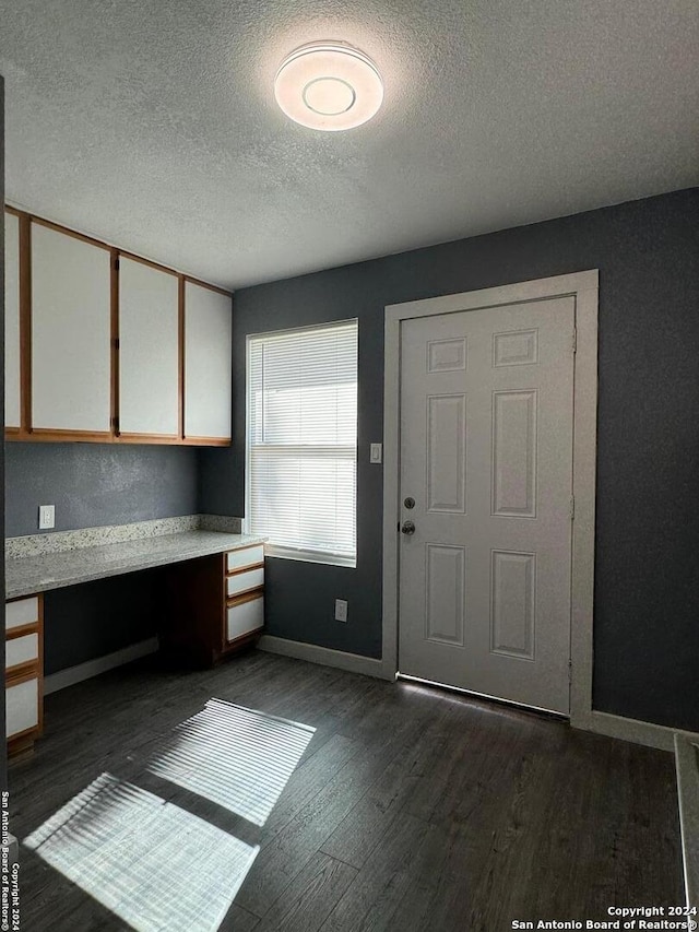 interior space with built in desk, dark hardwood / wood-style flooring, a textured ceiling, and white cabinetry