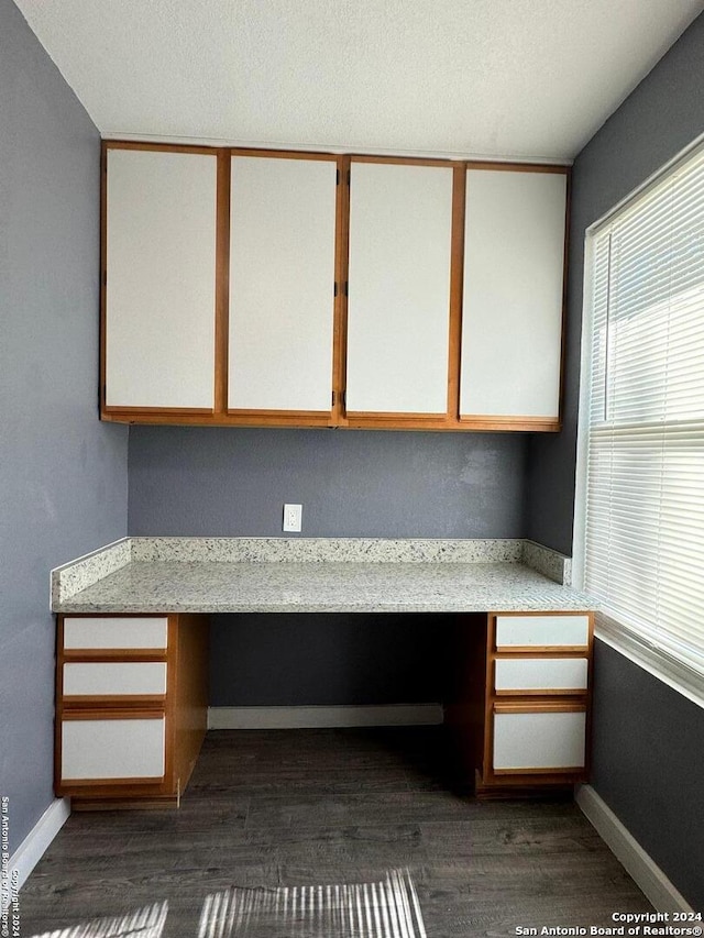 unfurnished office featuring built in desk and dark hardwood / wood-style flooring