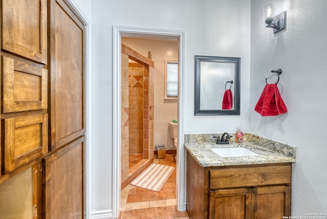 bathroom with tiled shower, tile floors, vanity, and toilet