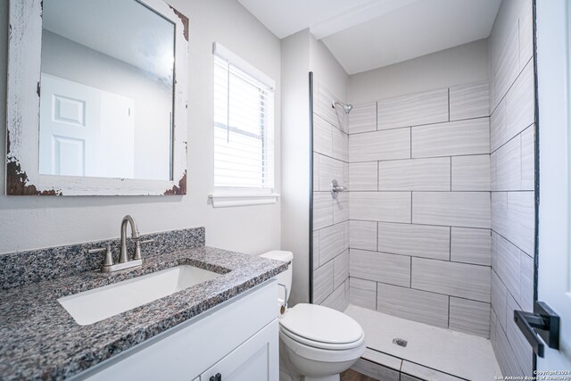 bathroom with a tile shower, vanity, and toilet