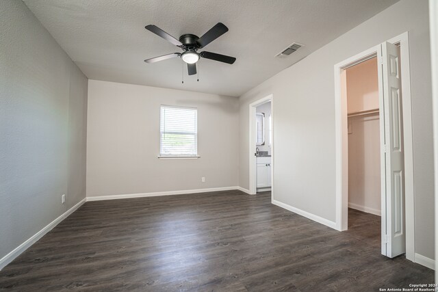 unfurnished bedroom featuring dark wood-type flooring, ceiling fan, a closet, and a spacious closet