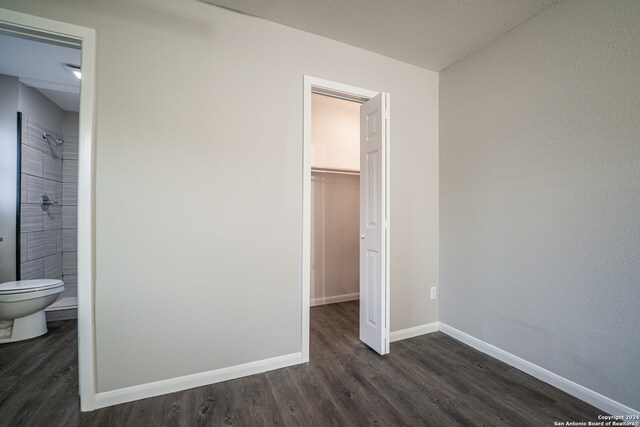 unfurnished bedroom with a spacious closet, dark wood-type flooring, a closet, and ensuite bath