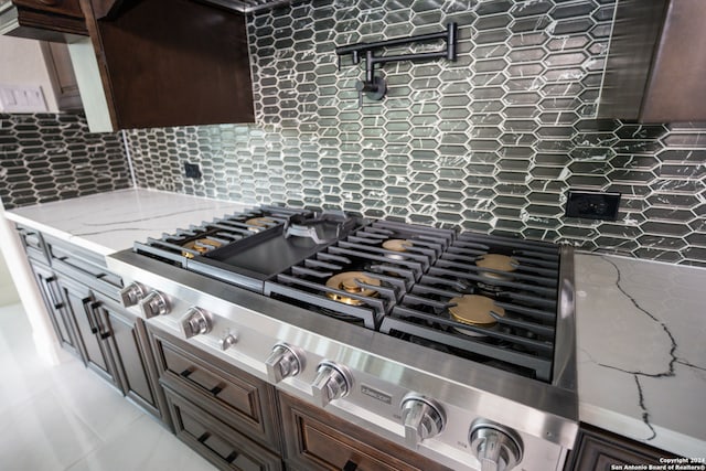 interior details featuring dark brown cabinetry, decorative backsplash, light stone countertops, and stainless steel gas cooktop