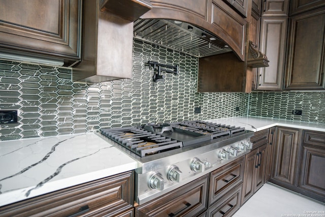 kitchen featuring dark brown cabinets, light stone counters, stainless steel gas cooktop, and tasteful backsplash