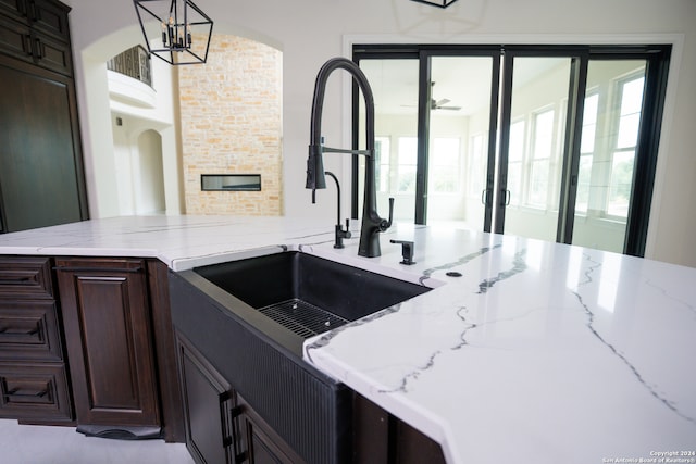 kitchen featuring dark brown cabinetry, sink, light stone counters, decorative light fixtures, and a fireplace