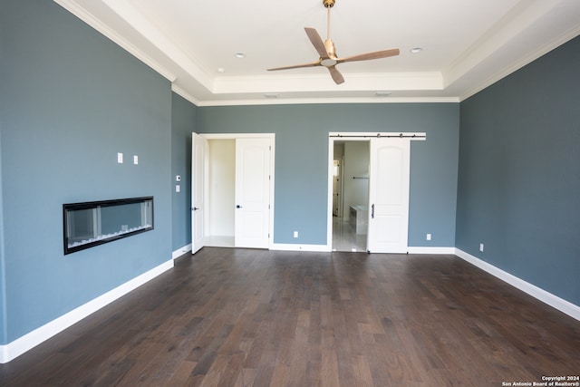 empty room featuring a raised ceiling, a barn door, ceiling fan, and dark hardwood / wood-style flooring