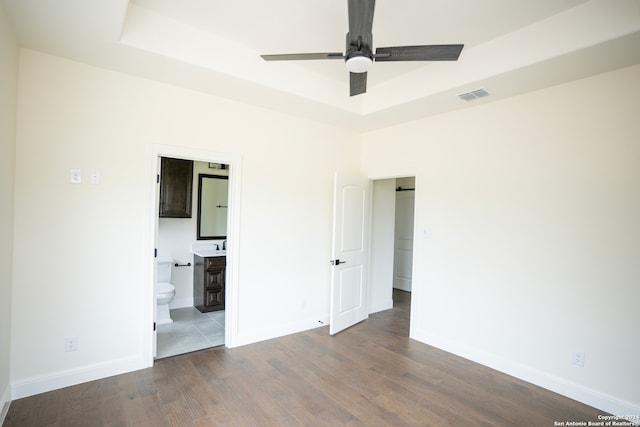 unfurnished bedroom featuring hardwood / wood-style flooring, ensuite bathroom, ceiling fan, and a tray ceiling