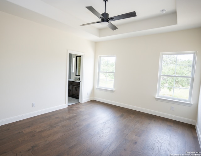 unfurnished bedroom with a tray ceiling, multiple windows, ensuite bathroom, and ceiling fan