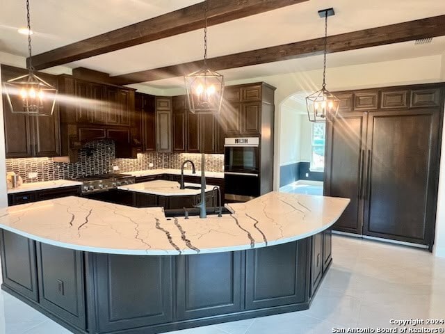 kitchen with a large island, beam ceiling, light stone countertops, and decorative light fixtures