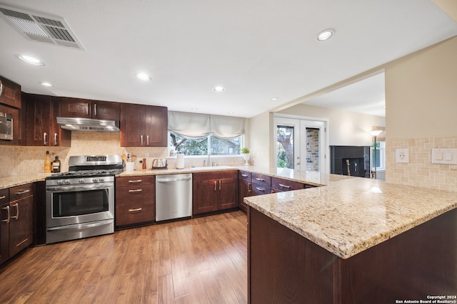 kitchen with stainless steel appliances, light hardwood / wood-style flooring, backsplash, and kitchen peninsula