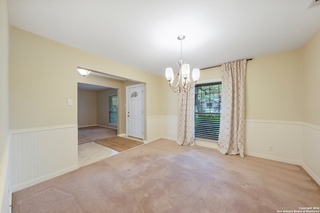 spare room featuring an inviting chandelier and light colored carpet