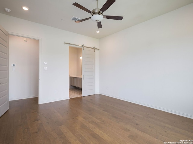 unfurnished bedroom featuring a barn door, ceiling fan, a closet, and dark wood-type flooring