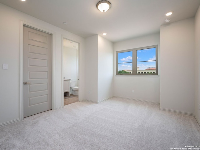 unfurnished bedroom featuring light carpet and connected bathroom