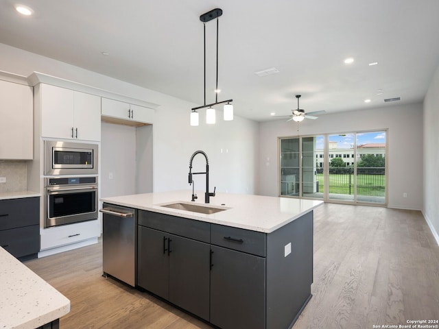 kitchen featuring light wood-type flooring, appliances with stainless steel finishes, pendant lighting, sink, and ceiling fan