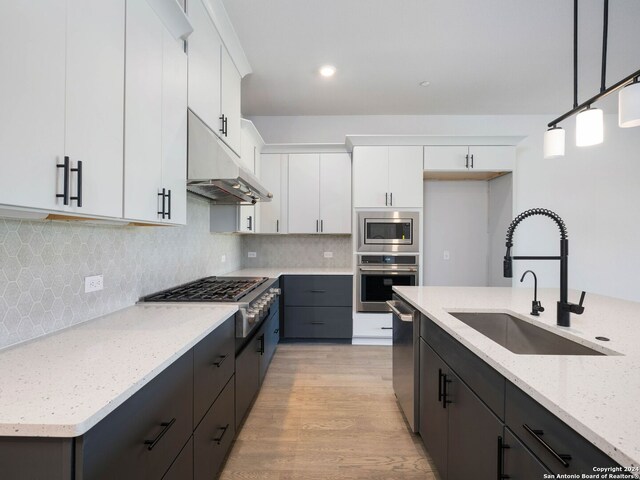 kitchen with light wood-type flooring, stainless steel appliances, white cabinets, sink, and tasteful backsplash