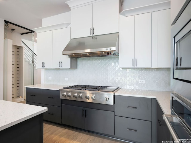 kitchen featuring light stone countertops, light wood-type flooring, appliances with stainless steel finishes, white cabinets, and backsplash