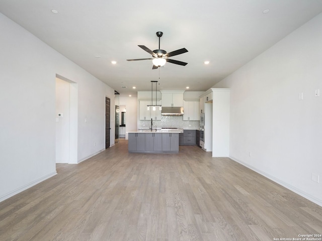 kitchen featuring ceiling fan, tasteful backsplash, a center island with sink, pendant lighting, and white cabinets