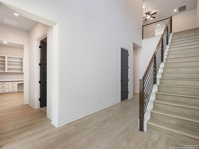 staircase with a towering ceiling, ceiling fan, and light hardwood / wood-style flooring