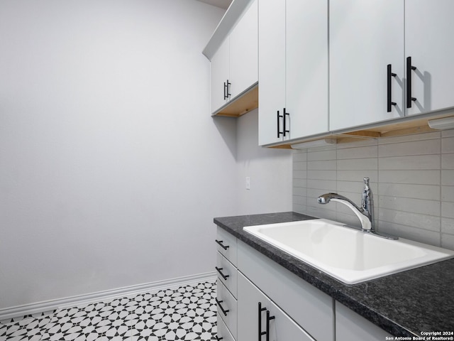 kitchen with sink, backsplash, white cabinetry, and light tile floors