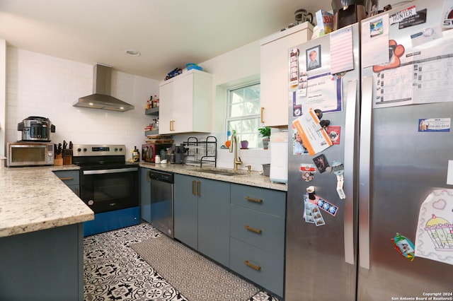 kitchen with wall chimney range hood, white cabinetry, stainless steel appliances, sink, and tasteful backsplash