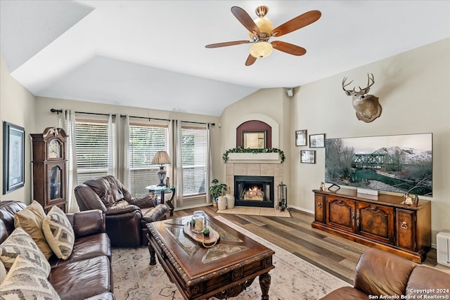 living room with ceiling fan, a tiled fireplace, vaulted ceiling, and wood-type flooring