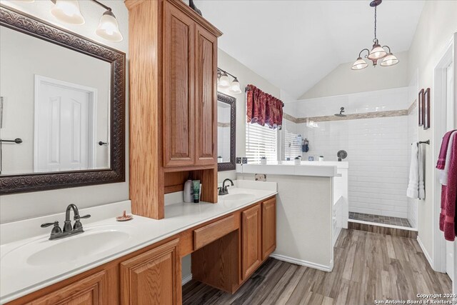 bathroom featuring lofted ceiling, a tile shower, hardwood / wood-style floors, and dual bowl vanity